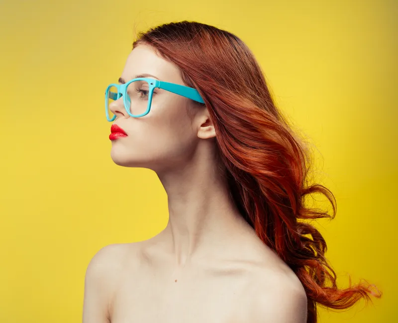 Женщина с обнаженными плечами, в синих очках и с рыжими волосами, кадрированное изображение