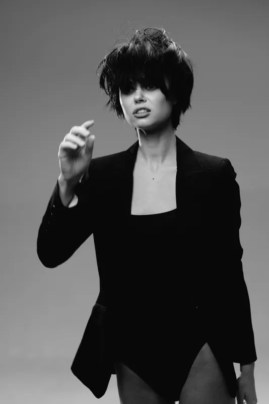 Black and white portrait of a stylish woman with short dark hair wearing a black blazer expressing confident attitude.