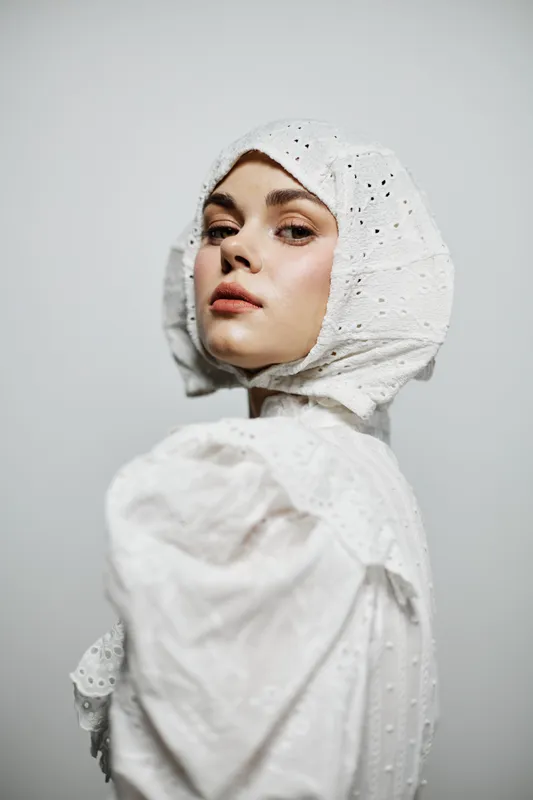 Portrait of an elegant young woman wearing a stylish white headscarf and blouse, captured against a minimalistic light background, exuding confidence and grace