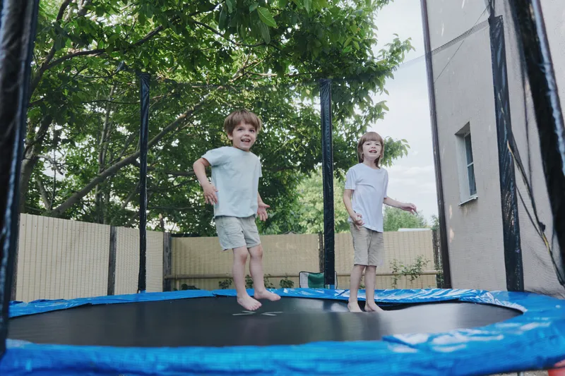 Happy kids jumping on a trampoline in a garden, surrounded by greenery and sunshine, bringing joy to summer afternoons.