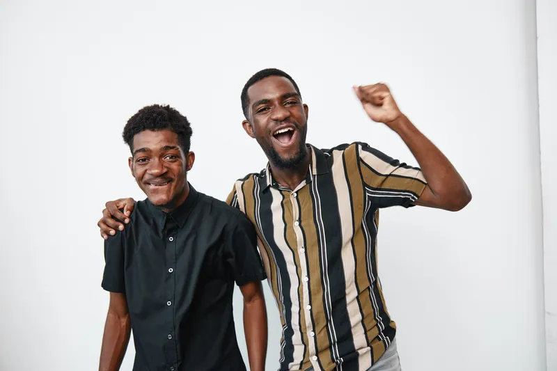 Two young black men with dark skin smiling and posing together in casual clothes on white background. Friends, happiness, joy and celebration with positive emotions and friendship.