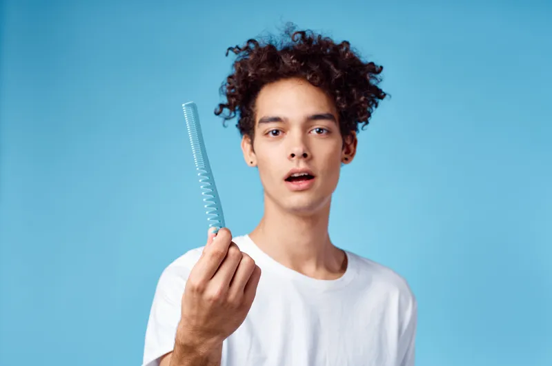Красивый парень с кудрявыми волосами на синем фоне, портрет крупным планом, спутанные локоны