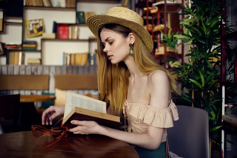 Симпатичная женщина в шляпе с книгой, читающая в интерьере, располагающем к отдыху