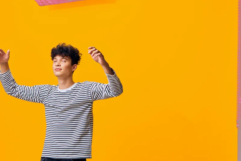 smiling man wearing striped shirt enjoying bright yellow background with playful and cheerful mood, casual style and youthful energy captured in studio lighting