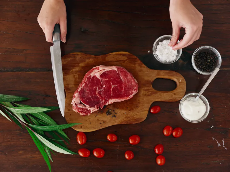 Женщина с ножом в руке нарезает свежее стейковое мясо для жарки на кухне