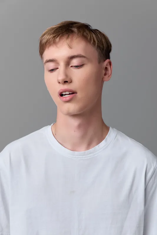 Face, expression, young man in white shirt, close up, head and shoulders, relaxed and candid mood, calm impression suitable for fashion, lifestyle, or editorial use with neutral background and soft
