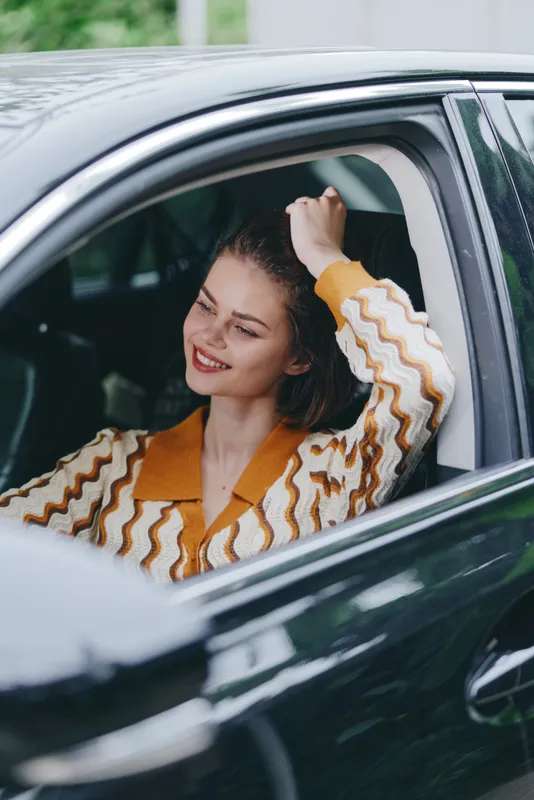 Smiling woman relaxing in a car, head resting near the window, enjoying a candid moment that showcases style, comfort, and confident charm.