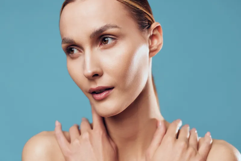 Woman portrait skincare beauty spa neck touch wellness closeup of adult woman with bare shoulders, hands at neck, calm expression, soft studio lighting, blue background