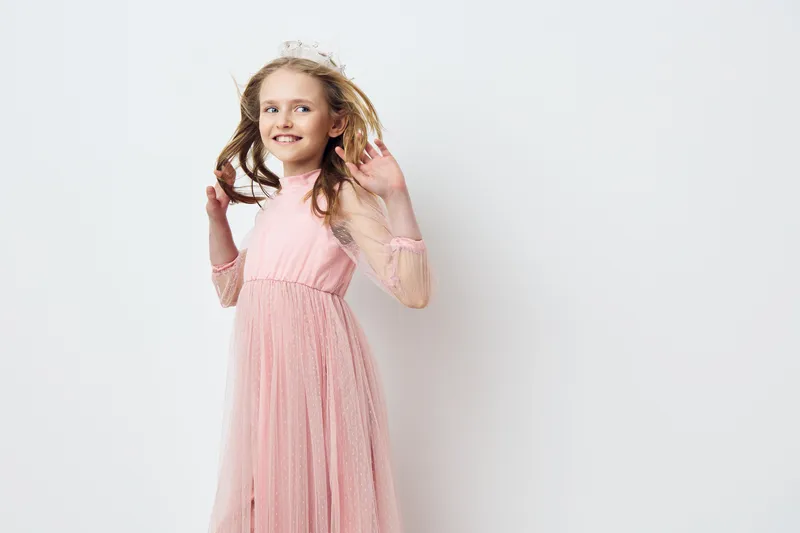 Joyful young girl in a light pink dress with flowing hair, exuding happiness against a minimalistic white background This cute child captures the essence of playfulness and innocence