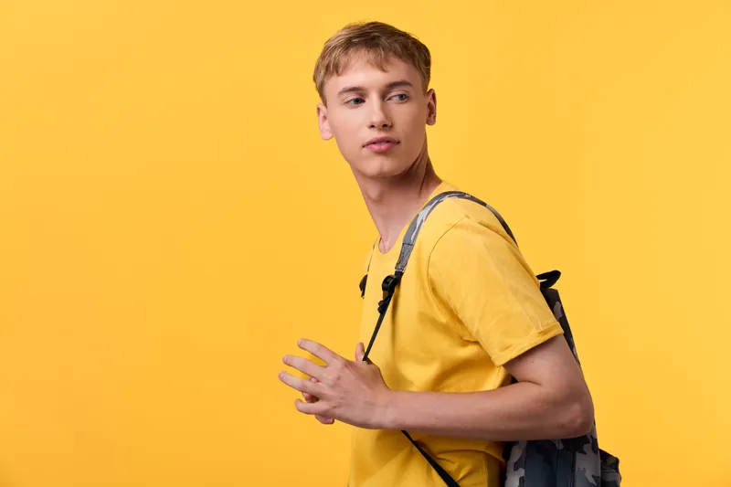 Man, young, backpack, yellow, shirt, studio, fashion, casual travel style captured in a bright monochrome setup with a thoughtful gaze, suggesting lifestyle, streetwear and everyday adventure for