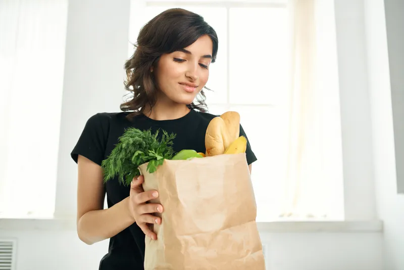 Женщина в черной футболке с пакетом продуктов: овощей, фруктов и здоровой пищи