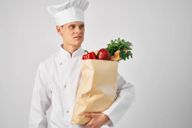 Шеф-повар с пакетом продуктов на кухне занимается приготовлением еды и работой