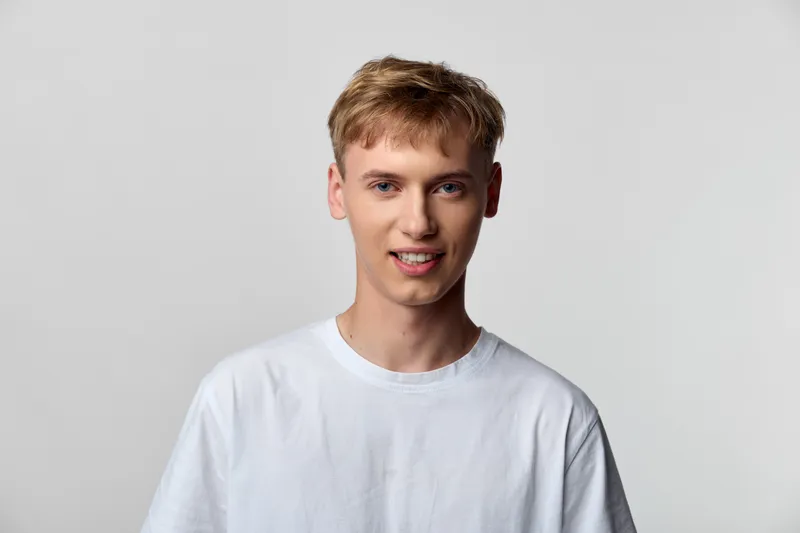 Young man in a white t shirt stands in a clean studio with a relaxed smile, casual fashion vibe, soft lighting and a neutral background suitable for lifestyle and fashion projects