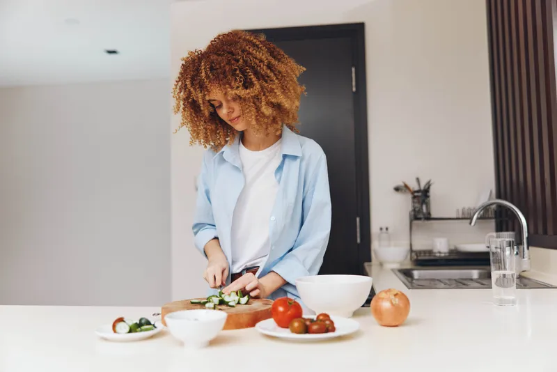 Привлекательная афроамериканка готовит вкусное блюдо на домашней кухне, основное внимание уделяется процессу приготовления
