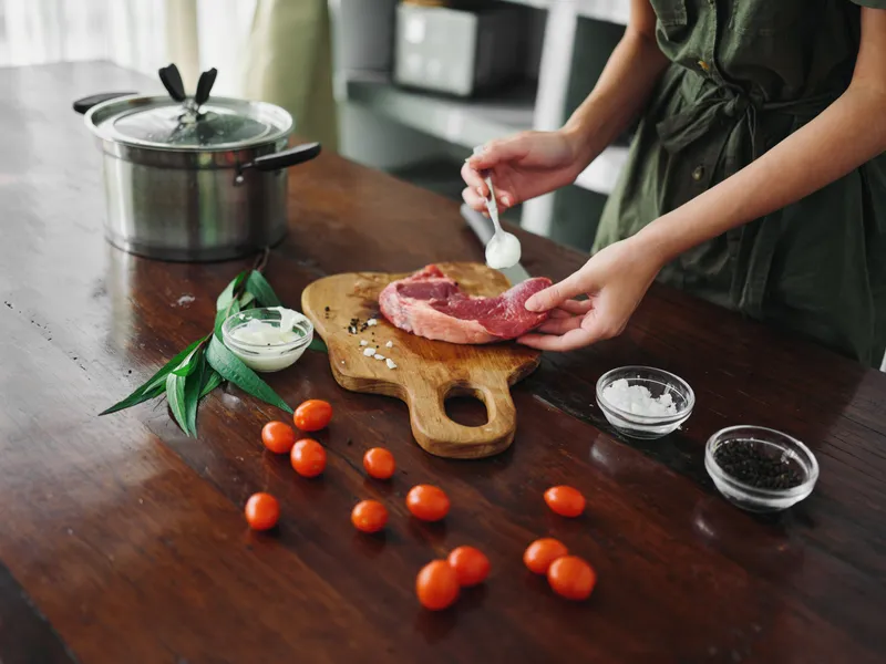 Женщина на кухне готовит ужин из мяса, овощей и специй на деревянном столе на фоне стильной кухни, крупным планом руки, свежие экопродукты, образ жизни