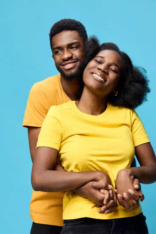 Happy young couple in matching yellow and orange t shirts posing against a bright blue background, showcasing joy, love, and togetherness