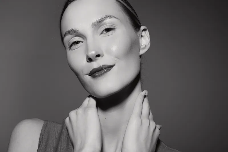 Young caucasian woman with fair skin poses confidently with hands on neck, smiling softly against a neutral background. Concept of beauty and self-confidence.