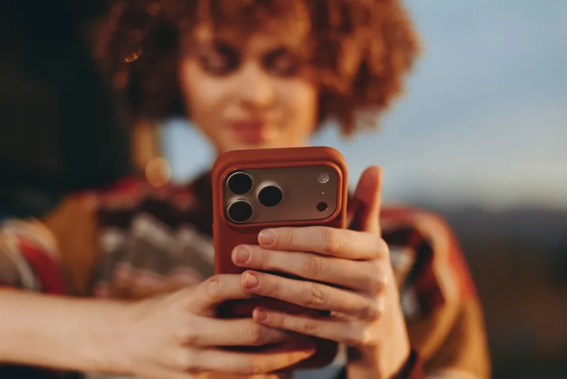 Woman smartphone selfie lifestyle outdoors sunset portrait curly hair, casual striped clothing holds phone close, soft bokeh background, warm evening light, relaxed social media moment