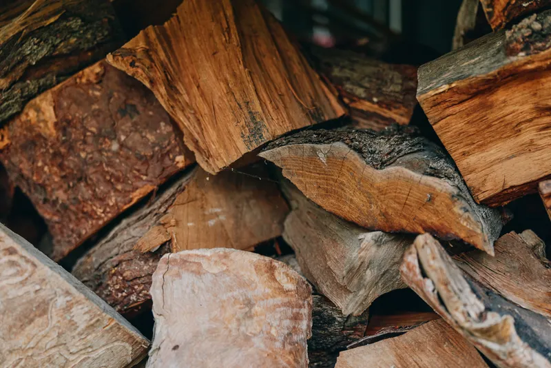 Firewood wood pile split logs stacked logs dry wood kindling in a rustic backyard closeup, textured seasoned oak and birch pieces for fireplace heating and cozy autumn atmosphere.