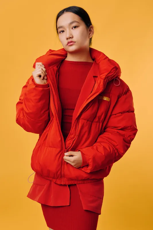 Young woman in red jacket and dress posing on yellow background, fashion style with casual warm clothing, confident model with long dark hair in studio lighting.