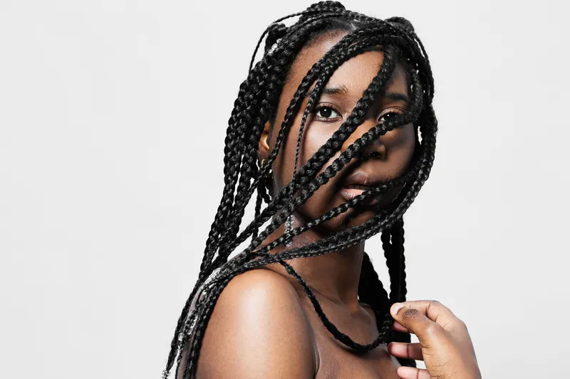 Portrait of a young Black woman with braided hair, showcasing natural beauty and expressive emotion against a minimalist white background