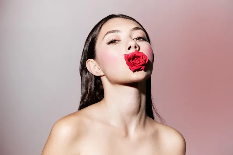 Идеальные чувственные губы: гламурная девушка в стиле Vogue с ярко-красной помадой на натуральном свежем фоне из роз