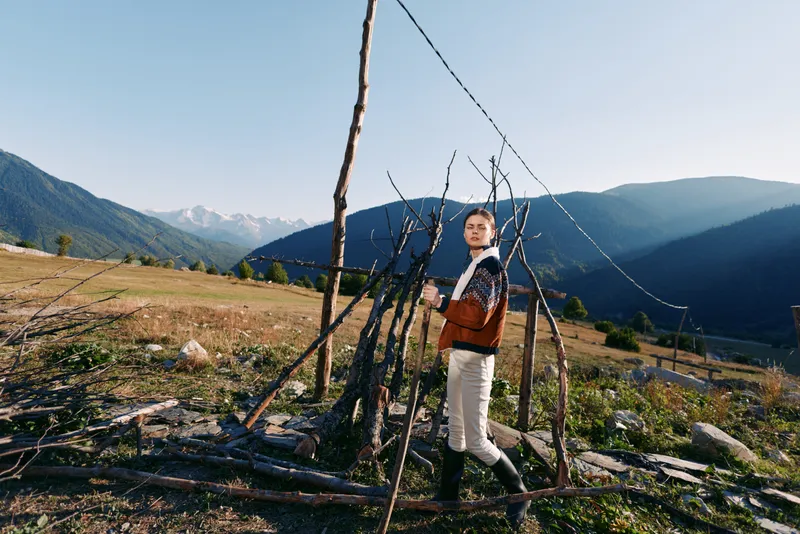 Woman in sweater and boots standing by a rustic fence in a rural field with mountains in the background, countryside landscape and clear sky for outdoor lifestyle travel