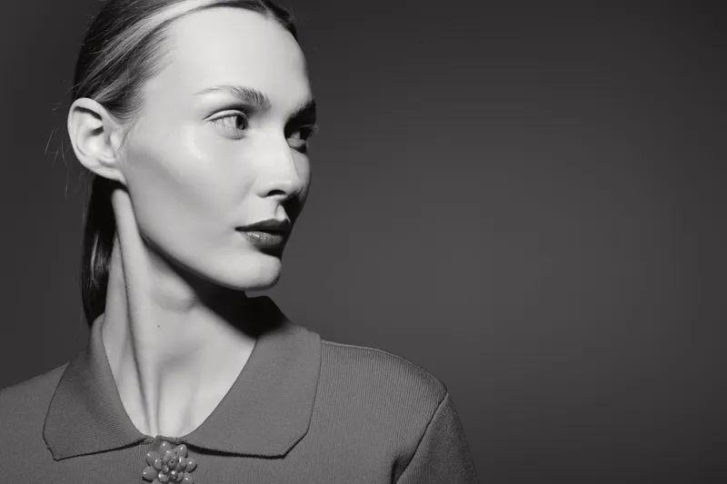 Elegant caucasian woman with pale skin and slicked back hair looks to the side wearing vintage style clothing. Monochrome portrait with soft lighting and minimalistic background.