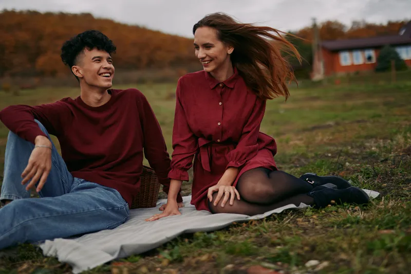A candid scene captures authenticity and credibility as friends laugh and relax on a picnic blanket, enjoying a cool autumn breeze under a mellow sky with warm tones.