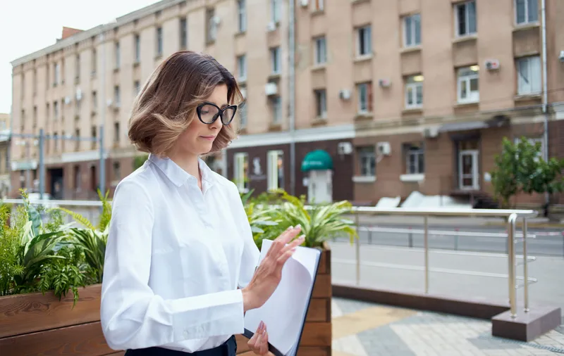 Женщина на улице возле цветов показывает документы в папке