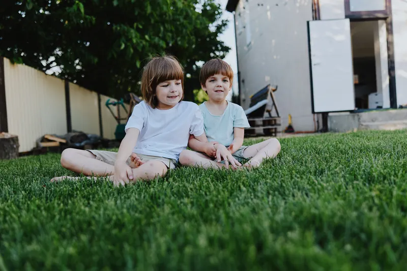 Two cheerful children sitting on green grass, enjoying a sunny day. Their playful expressions capture the essence of childhood joy and innocence.