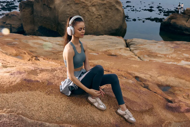 Young woman with headphones enjoying nature on rocky beach, wearing athletic wear and expressing tranquility, ideal for fitness and relaxation concepts