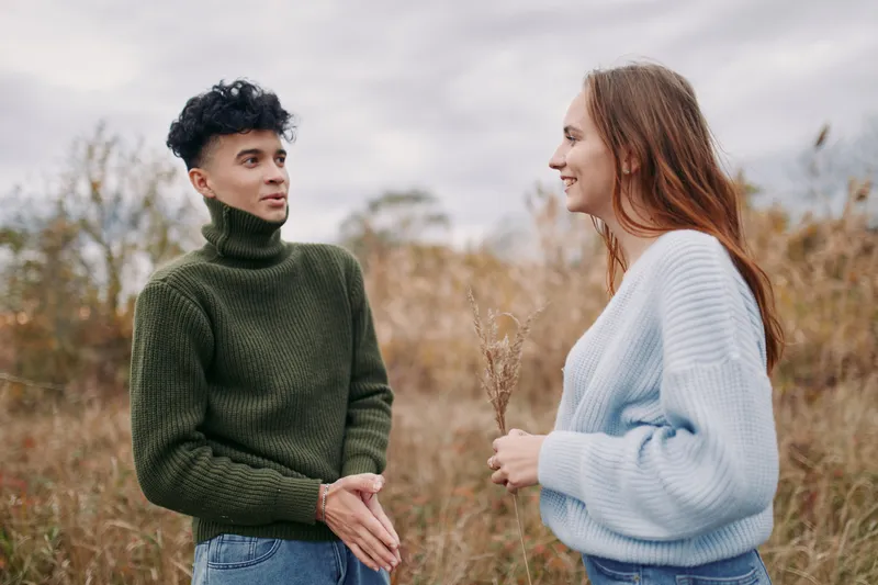 Two young adults share a sincere conversation in an autumn meadow, making steady eye contact and showing relaxed body language. Natural facial expressions convey genuine connection and dependable