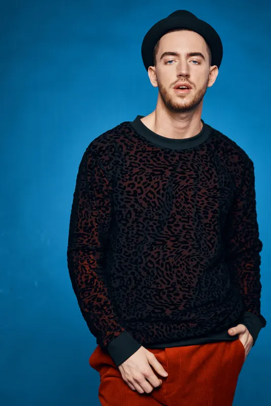 Красивый мужчина в черном свитере позирует в современной одежде на синем фоне