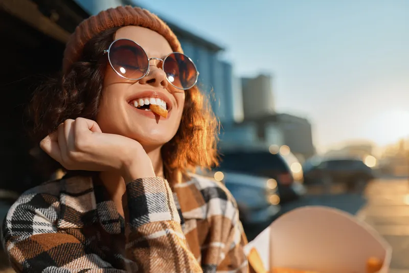 Woman portrait smile fries sunglasses golden candid urban enjoying sunset street food, authenticity and candid lifestyle vibe with golden hour glow, mindful living and emotional storytelling.