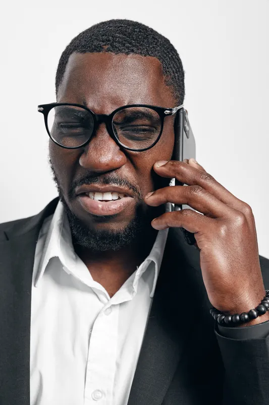 African American man with dark skin wearing glasses and suit talking on smartphone with serious expression in studio. Business communication and technology concept.