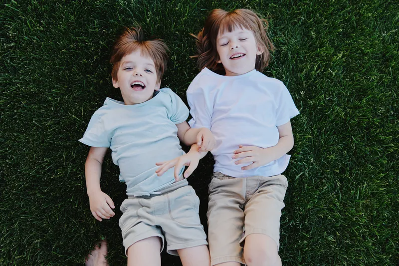 Happy children lying on green grass, enjoying a sunny day outdoors. Their joyful expressions reflect carefree moments of childhood and playfulness.