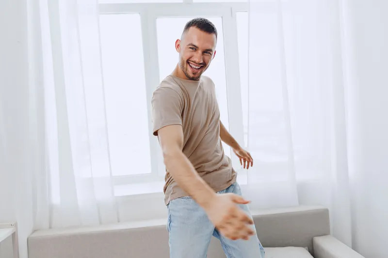 Happy man smiling at home during a digital detox, embracing a moment of authentic imperfection and soft masculinity in a serene environment.
