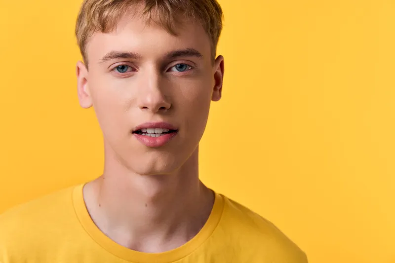 Young male with a bright yellow background and yellow shirt, close up face in studio lighting, clean composition, vivid color, and expressive gaze.