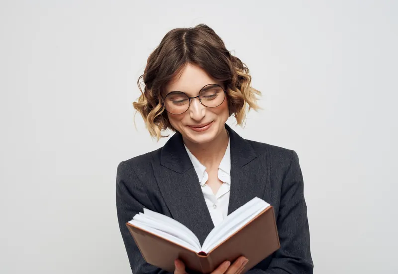 Женщина в классическом костюме с открытой книгой и очками на лице, обрезанный вид