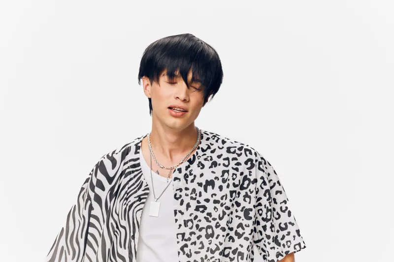 young man wearing animal print shirt with black and white pattern posing confidently against plain white background