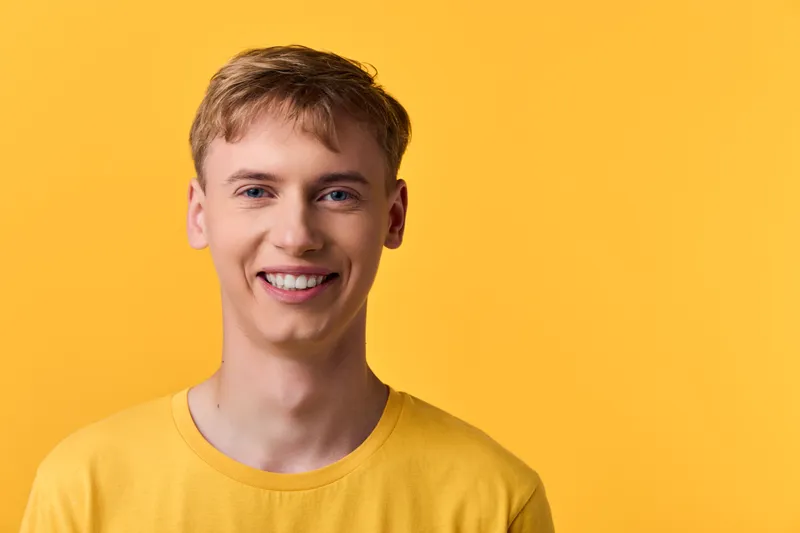 Smiling young male wearing a bright yellow t shirt against a vibrant yellow backdrop, capturing friendly, casual studio style and warm, approachable mood for lifestyle, marketing and product imagery.