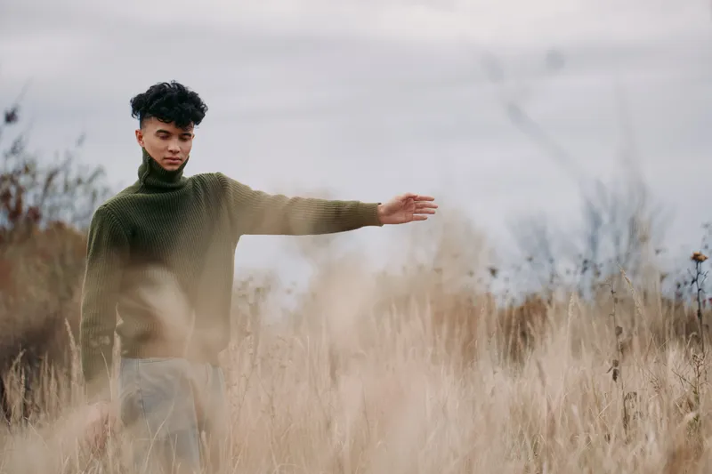 Authenticity in frame shows a young man standing in tall grass, arms open, conveying sincerity, balance, and a grounded connection with nature.