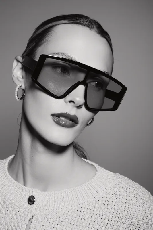 Young white woman with pale skin and slicked hair wearing large sunglasses and earrings in a studio portrait. Fashion and beauty concept.