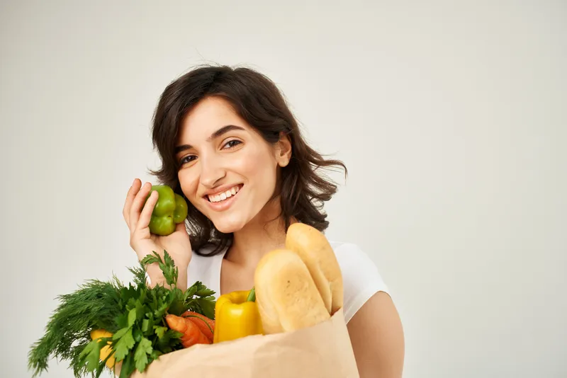 Улыбающаяся женщина с пакетом продуктов в супермаркете на светлом фоне