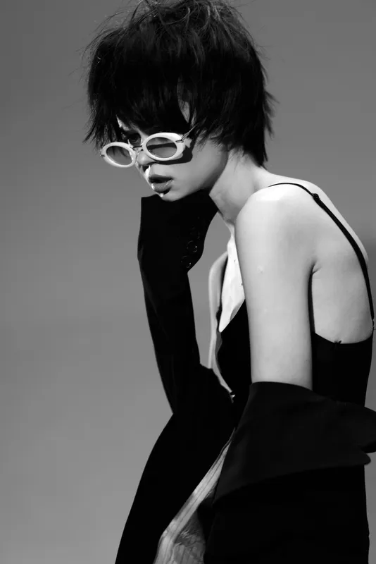 Black and white portrait of stylish woman with short hair wearing white glasses and black outfit in modern fashion concept