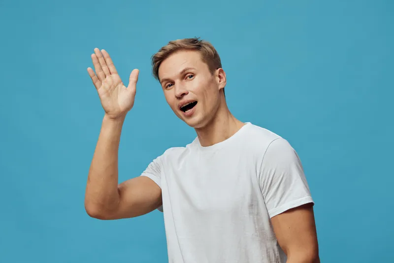 young smiling man waving hand happy caucasian person in white t-shirt isolated blue background digital nomad communication concept