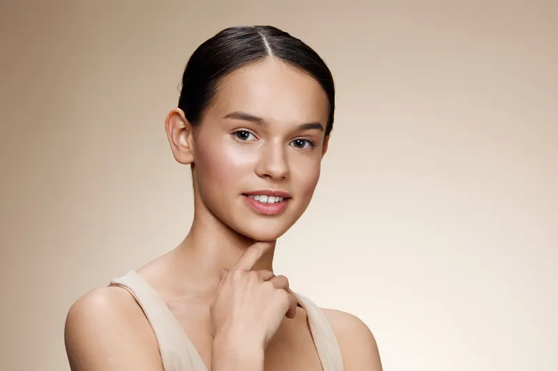 Beautiful young woman with natural makeup and neutral background, showcasing clear skin, graceful pose, and a confident smile, reflecting beauty and self care