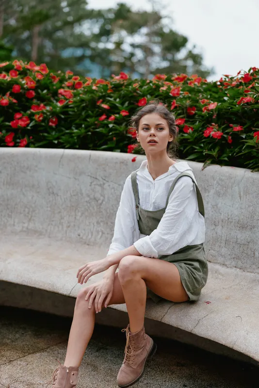 Young woman in casual outfit sitting on a bench, surrounded by vibrant flowers, expressing calmness and confidence in a natural setting