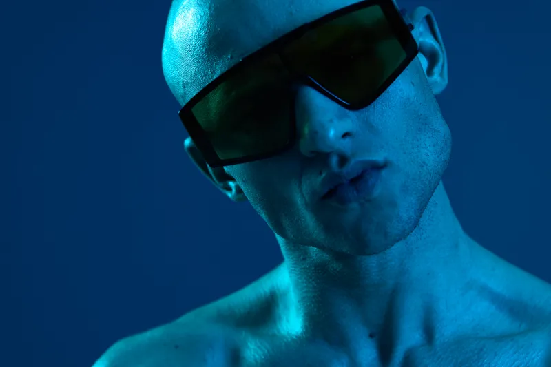 Stylish man with sunglasses poses against a blue background, creating a vibrant, contemporary atmosphere. Captures a unique blend of fashion and art.